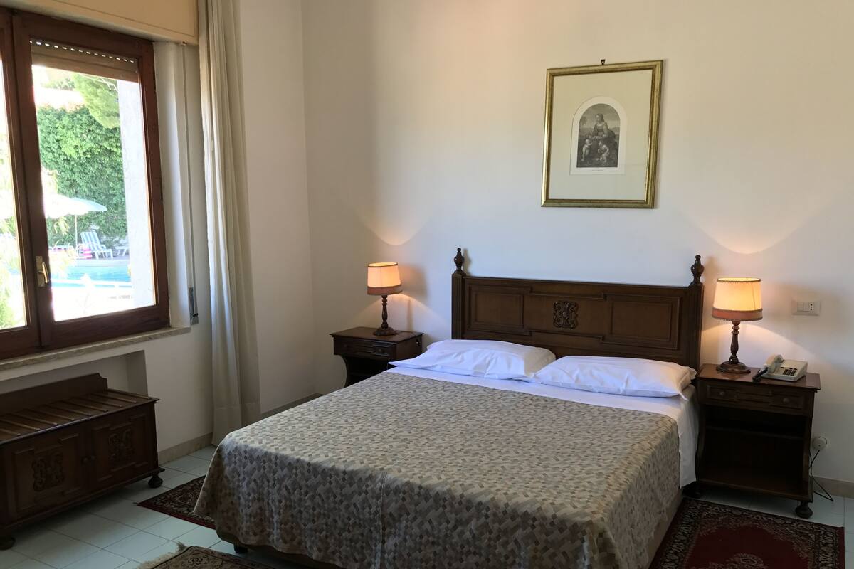 A neatly arranged bedroom with a bed, two bedside tables with lamps, a framed picture on the wall, and a window with curtains.