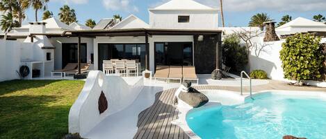A modern villa with a pool, outdoor seating, and a stone wall.