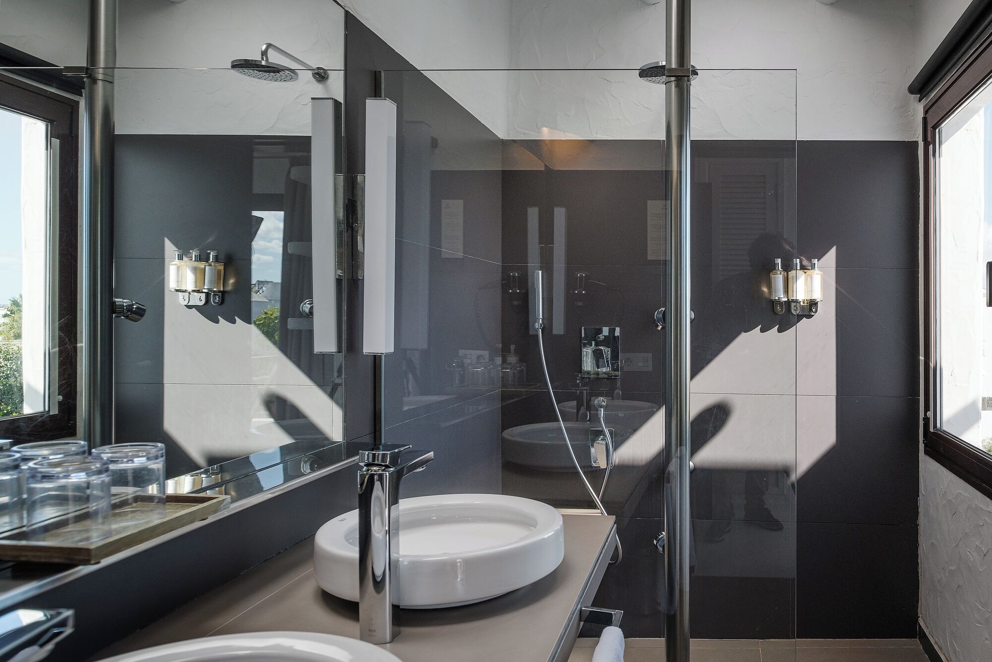 A modern bathroom with a glass shower enclosure, a round sink, and a large mirror.