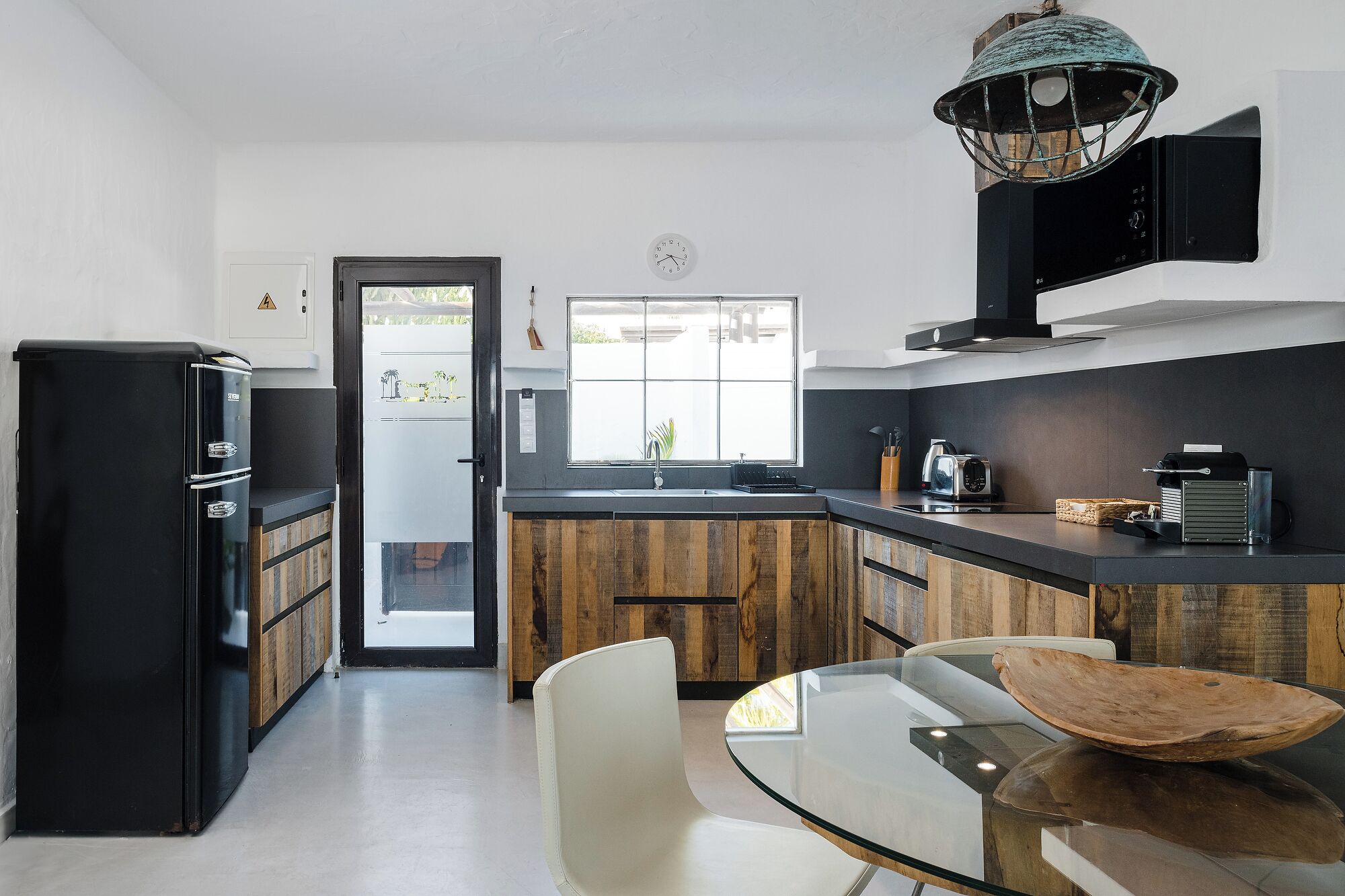 Una cocina moderna con un refrigerador negro, armarios de madera, una mesa de comedor de vidrio y un ventanal grande.