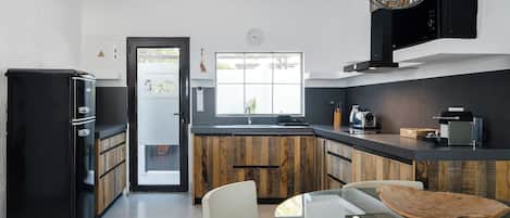 Una cocina moderna con un refrigerador negro, armarios de madera, una mesa de comedor de vidrio y un ventanal grande.