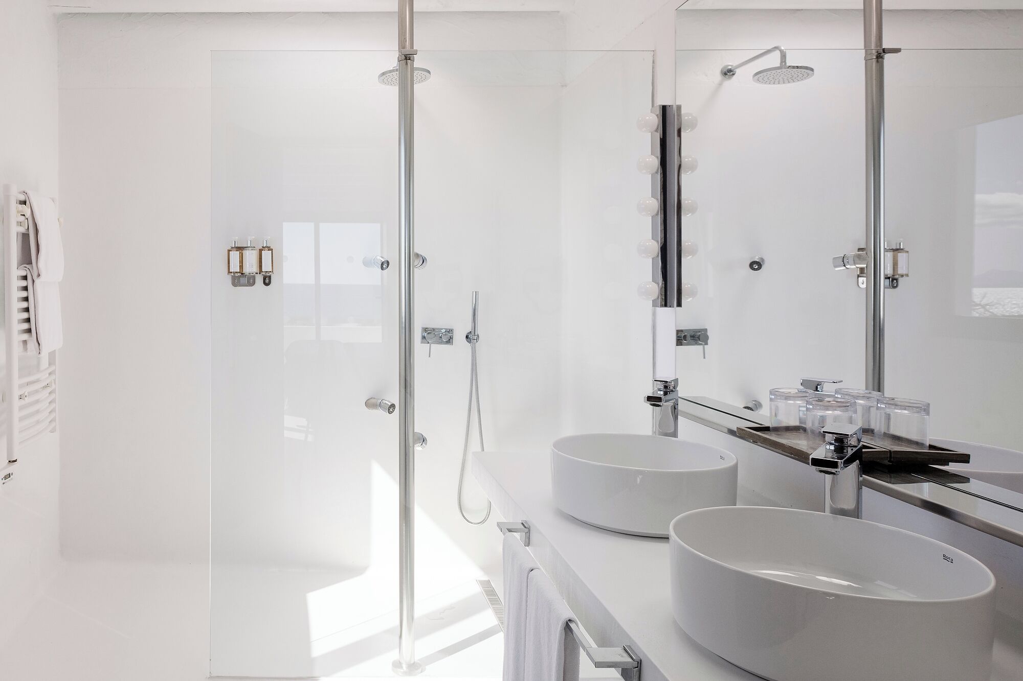 Un baño moderno con dos lavamanos redondos, ducha con cerramiento de vidrio y un espejo grande.
