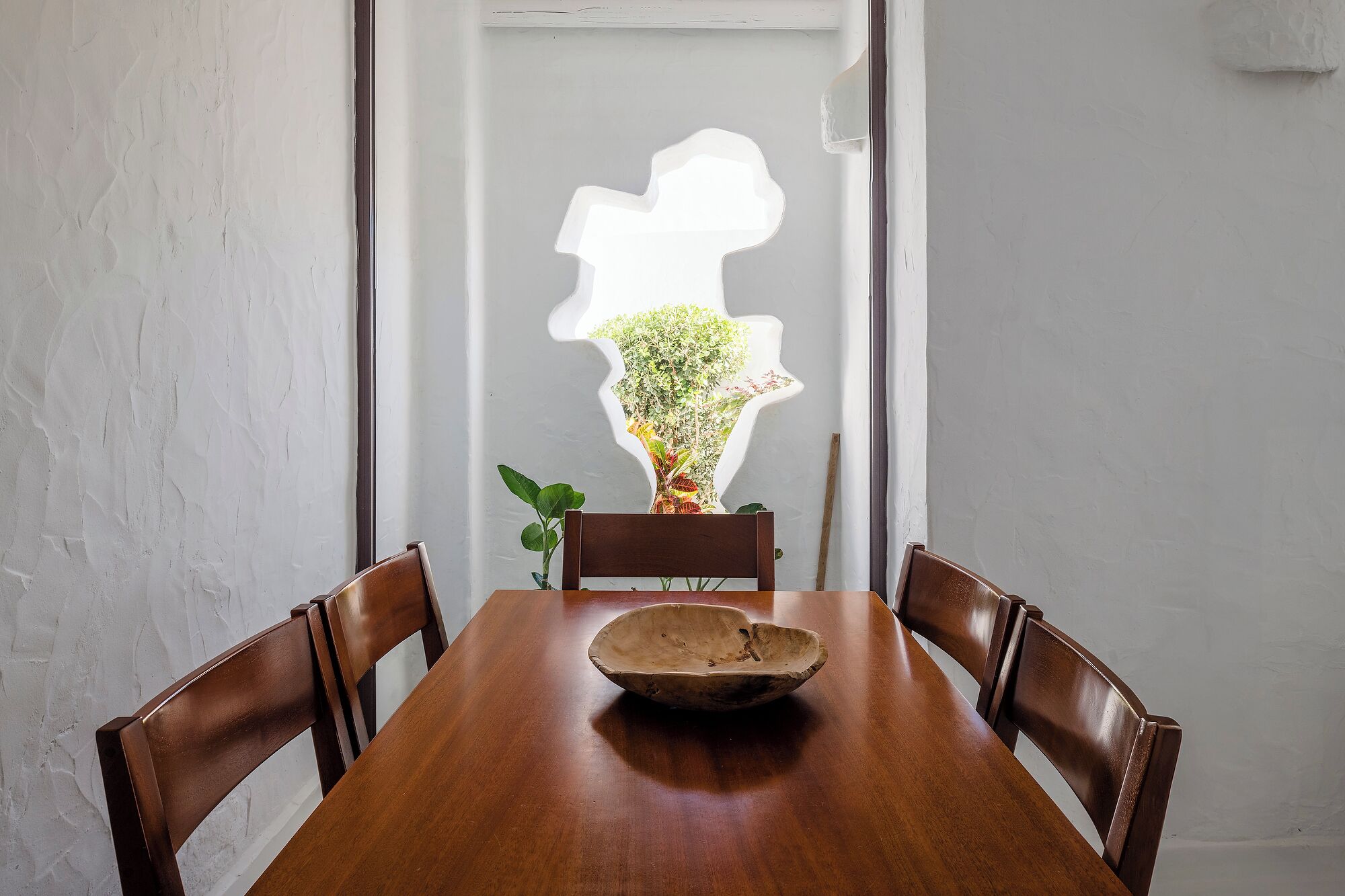 Ein Holztisch mit vier Stühlen, eine Vase mit Blumen und eine Wand mit strukturierter Oberfläche.