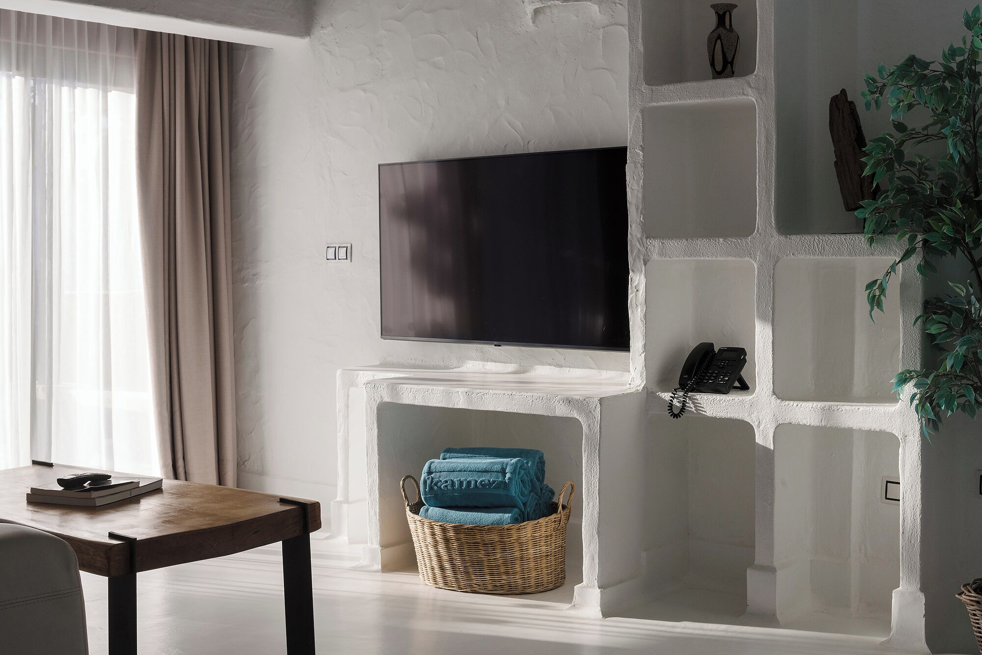 A living room with a flat-screen TV, a wooden table, a wicker basket with towels, and a plant.