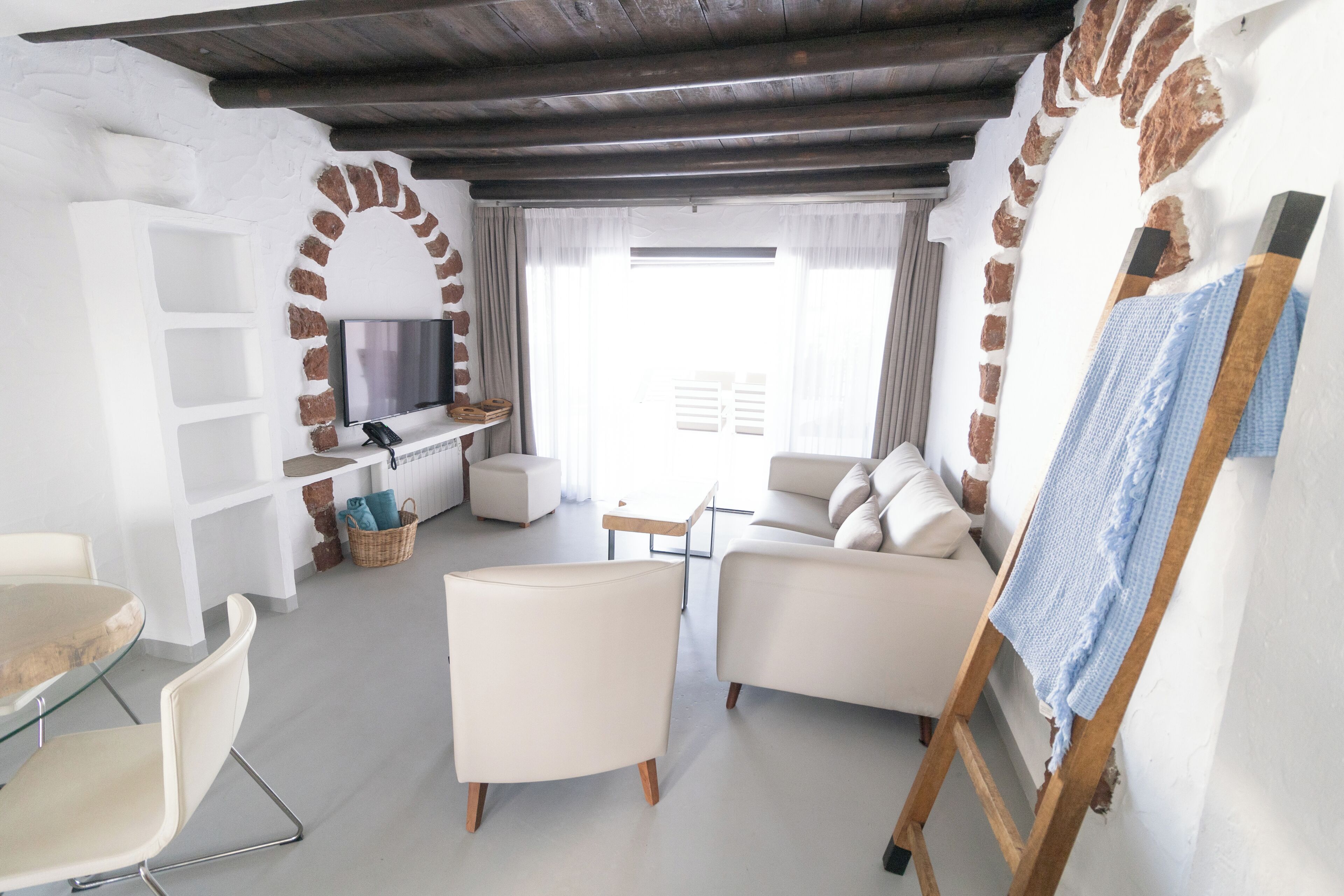 A modern living room with a fireplace, white sofas, a TV, and a wooden ladder.