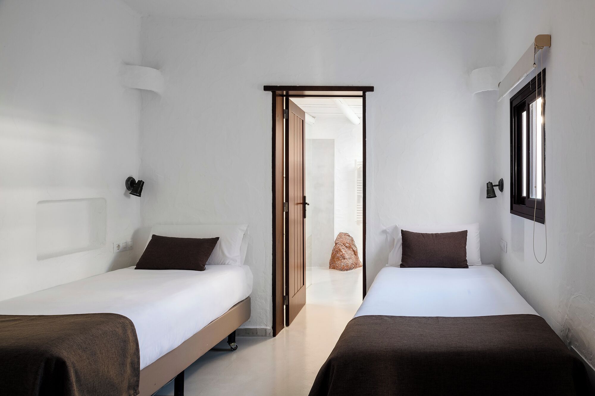 Une chambre d’hôtel avec deux lits simples, une porte en bois et une fenêtre avec un rideau.