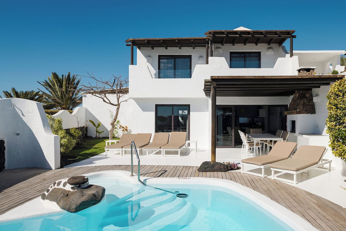 Ein modernes, zweistöckiges Haus mit Swimmingpool, Liegestühlen und einer Terrassenanlage.