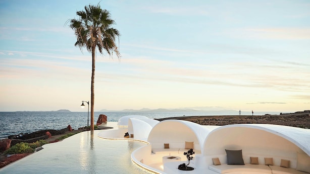 Un complexe hôtelier moderne doté d’une piscine, d’une architecture blanche et d’un palmier.