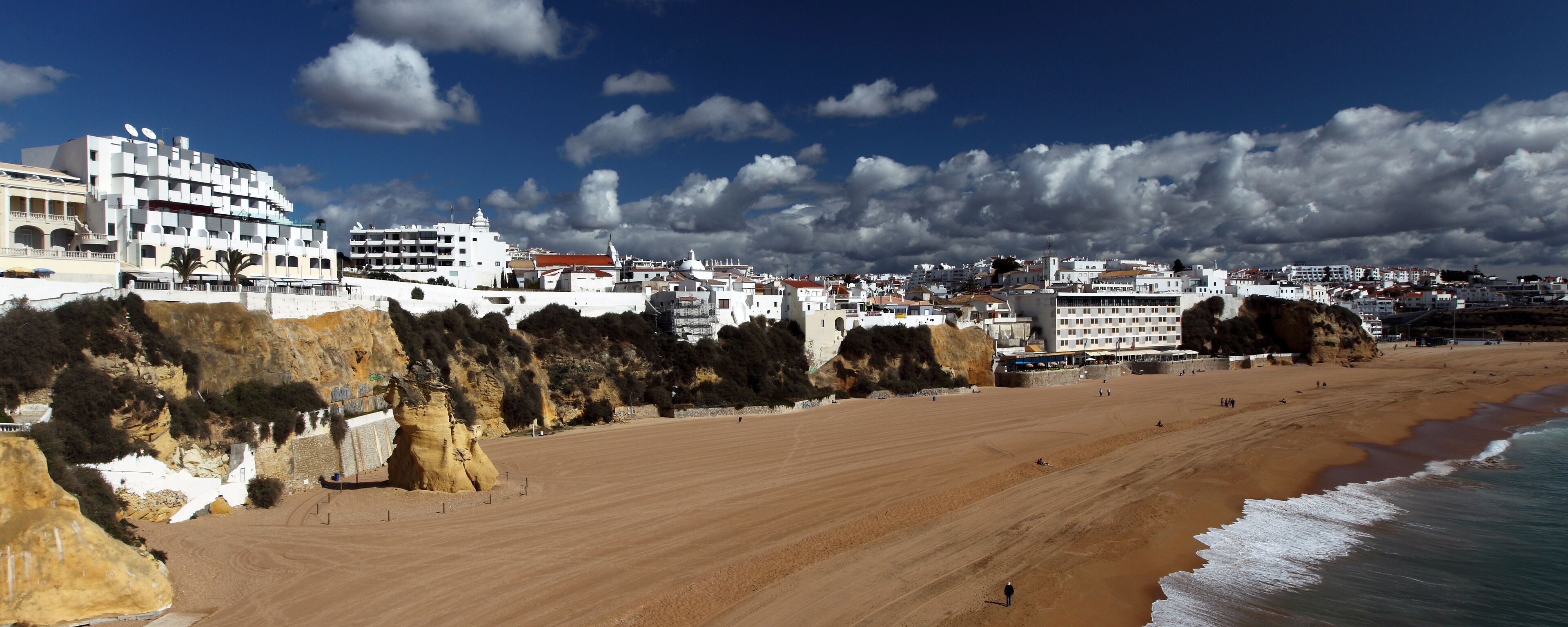 A coastal town with a sandy beach, white buildings, and rocky cliffs.