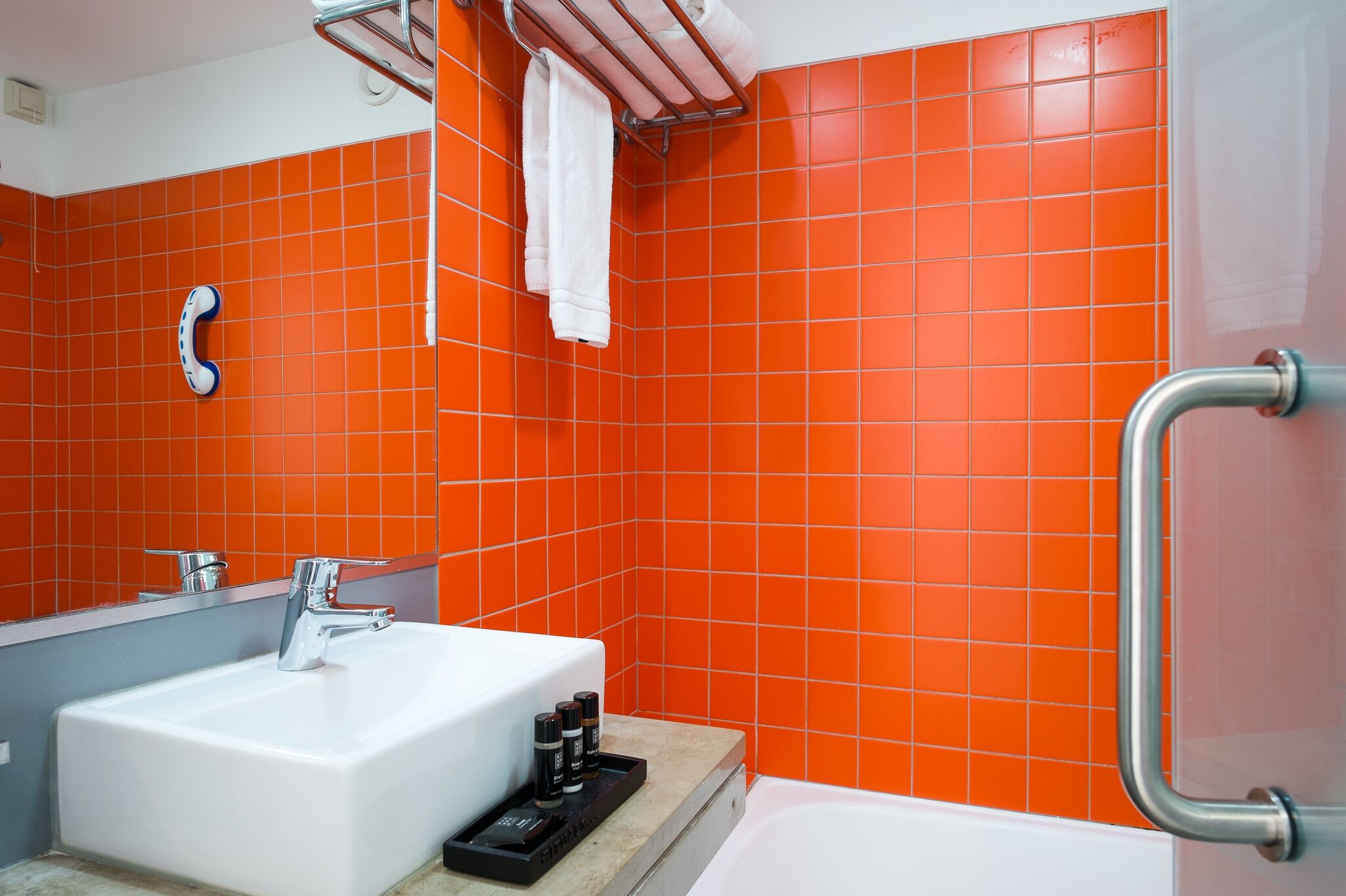 Un baño con un lavabo blanco, un espejo y paredes de azulejos naranjas.