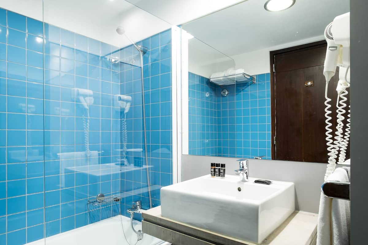 A modern bathroom with blue tiles, a white sink, and a hairdryer on the wall.