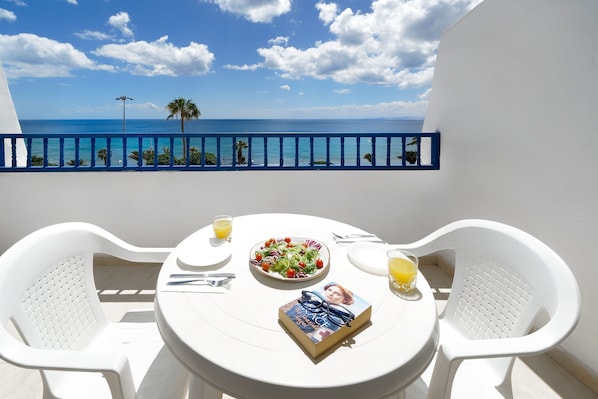 Varanda com mesa posta para dois, um livro, uma salada e dois copos de suco de laranja.