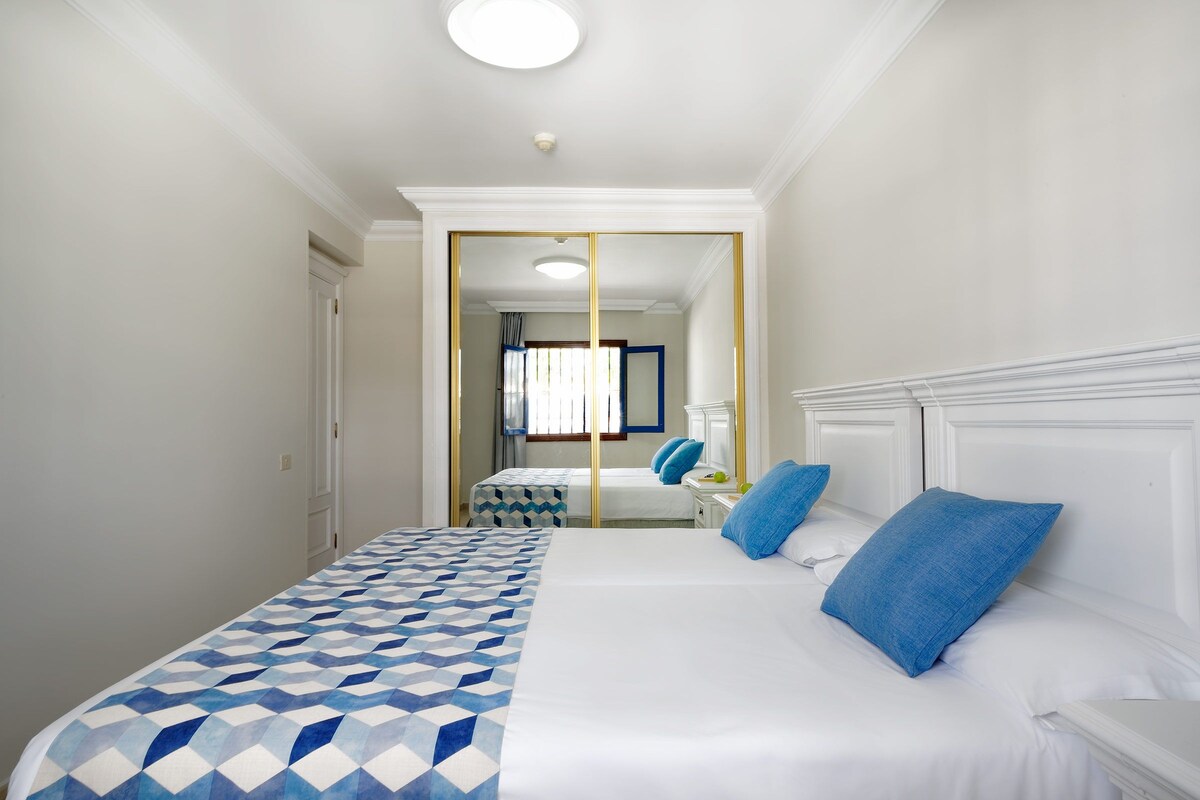 A hotel room with a large bed, a mirror, and a view of the hallway.