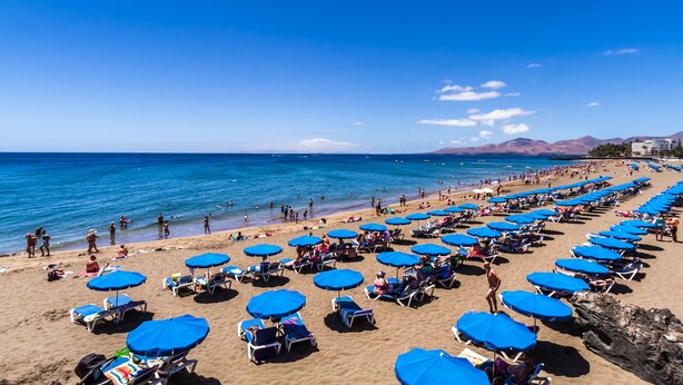 Una playa con hileras de sombrillas azules y tumbonas.