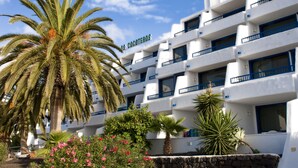 Un hotel de varios pisos con balcones, palmeras y plantas con flores en primer plano.