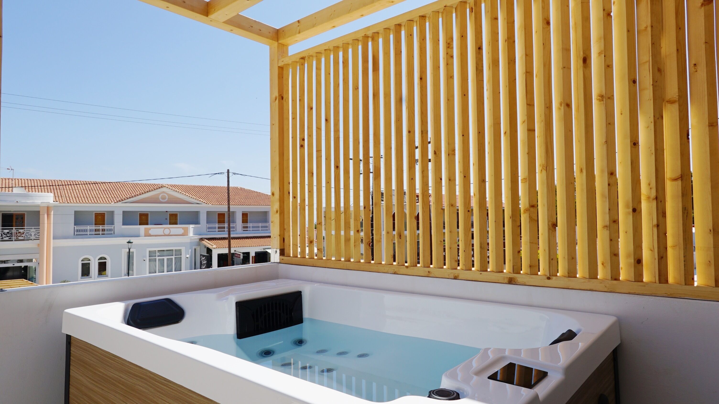 A balcony with a wooden slat screen, a white bathtub, and a view of buildings with a tiled roof.
