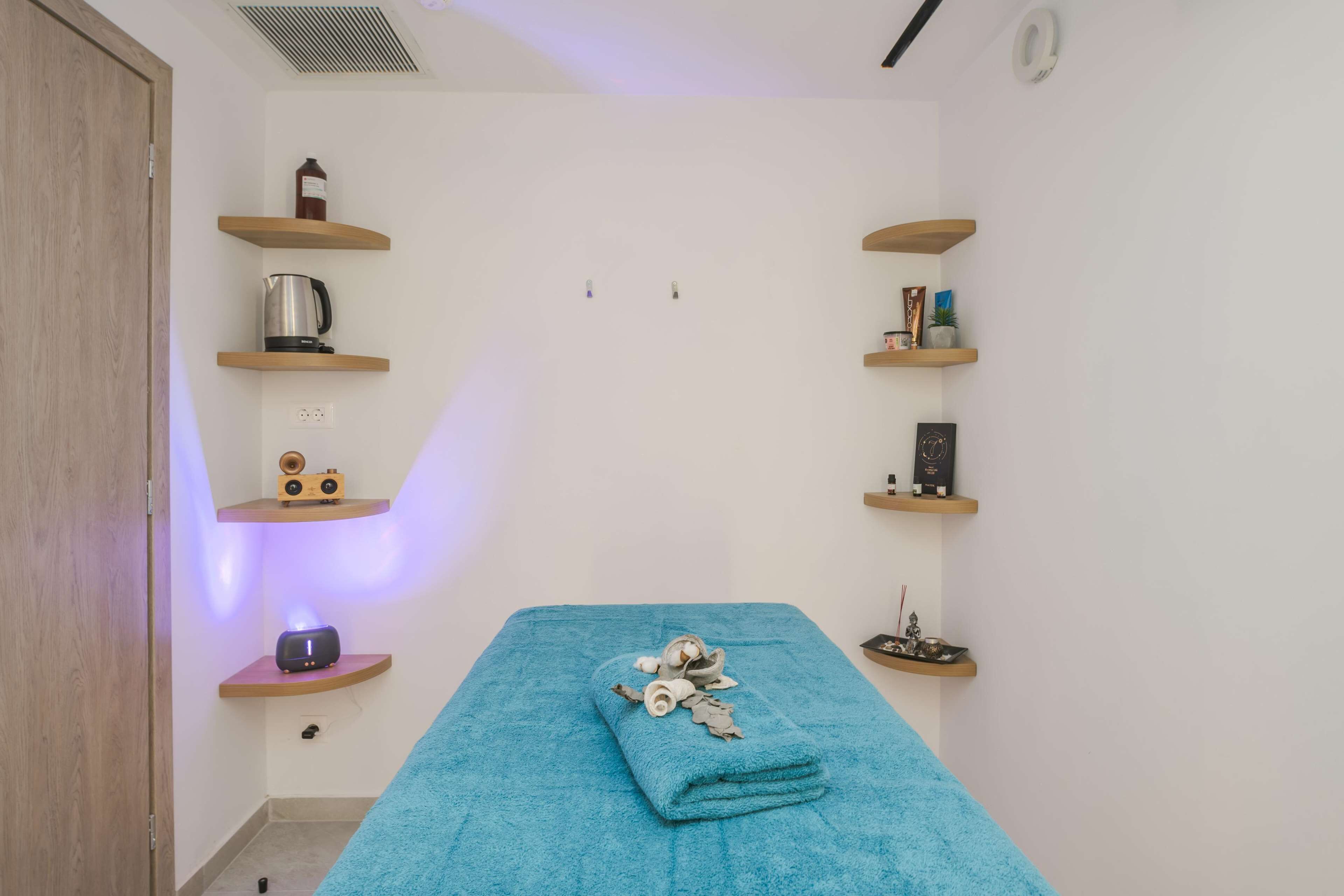 A room with a blue towel on a bed, wooden shelves with various items, and a wooden door.