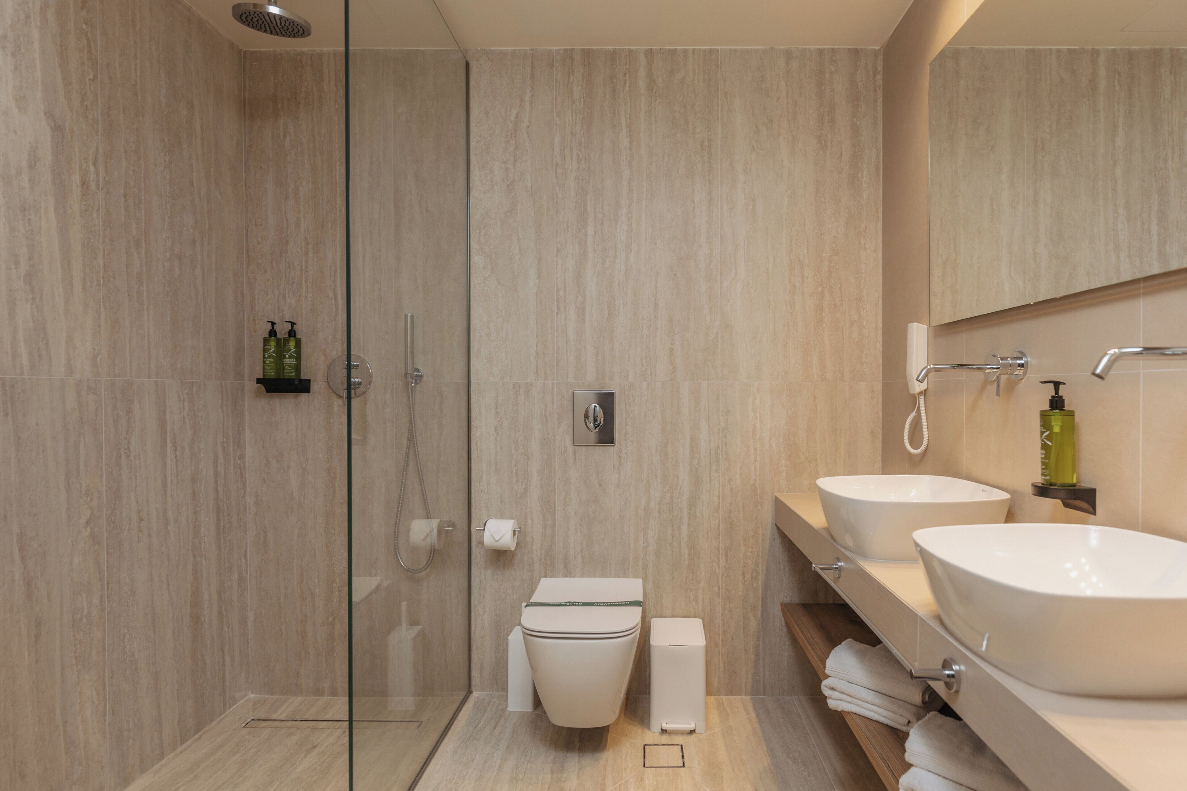 Un baño moderno con cabina de ducha de vidrio, dos lavamanos, un inodoro y un perchero para toallas.
