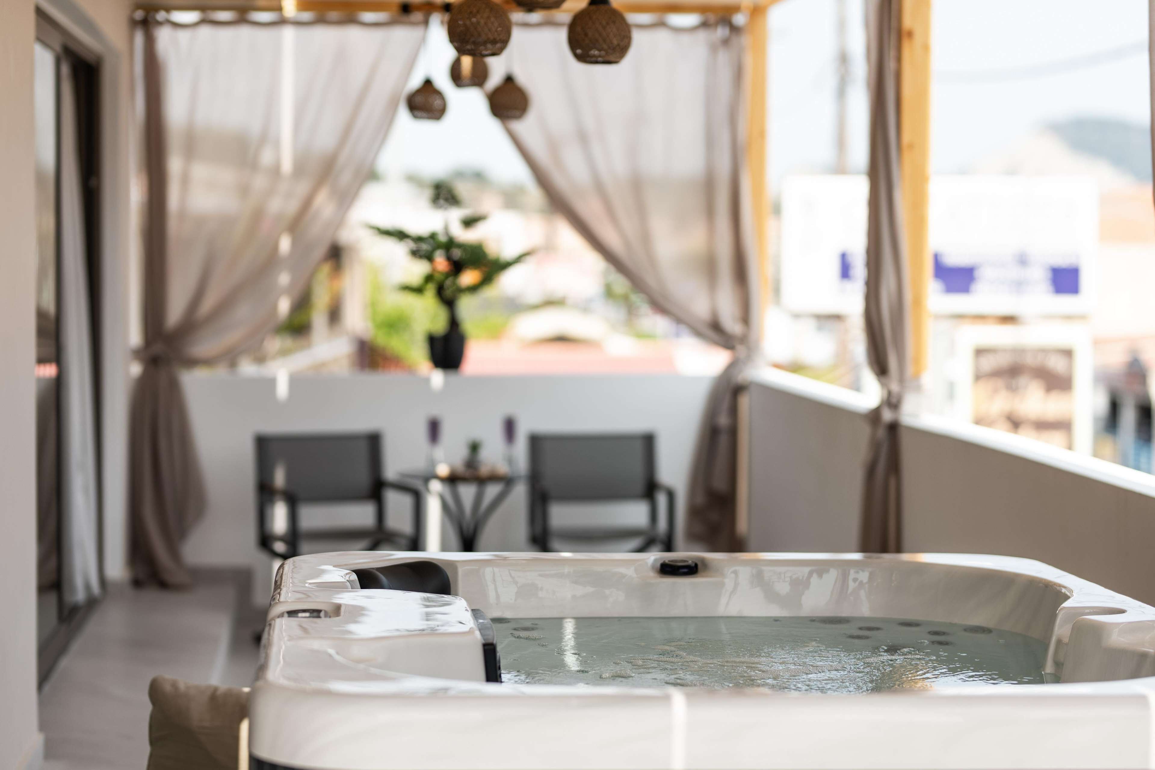 A hot tub in a room with a view, curtains, and a table with chairs.