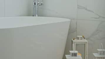 Een badkamer met een vrijstaand bad, witte marmeren tegels en twee verlichte witte lantaarns op de vloer.