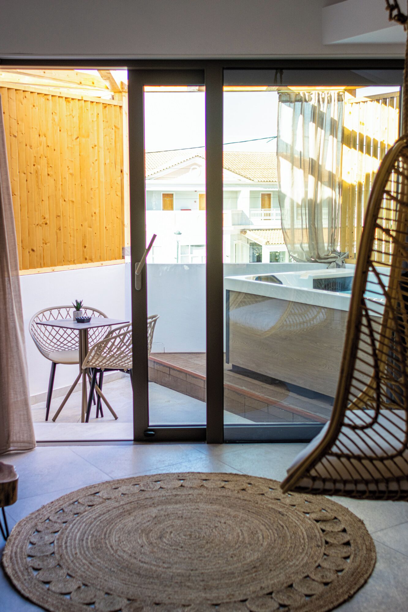 A room with a sliding glass door leading to a balcony, a woven rug, a wicker chair, and a small table with a plant.