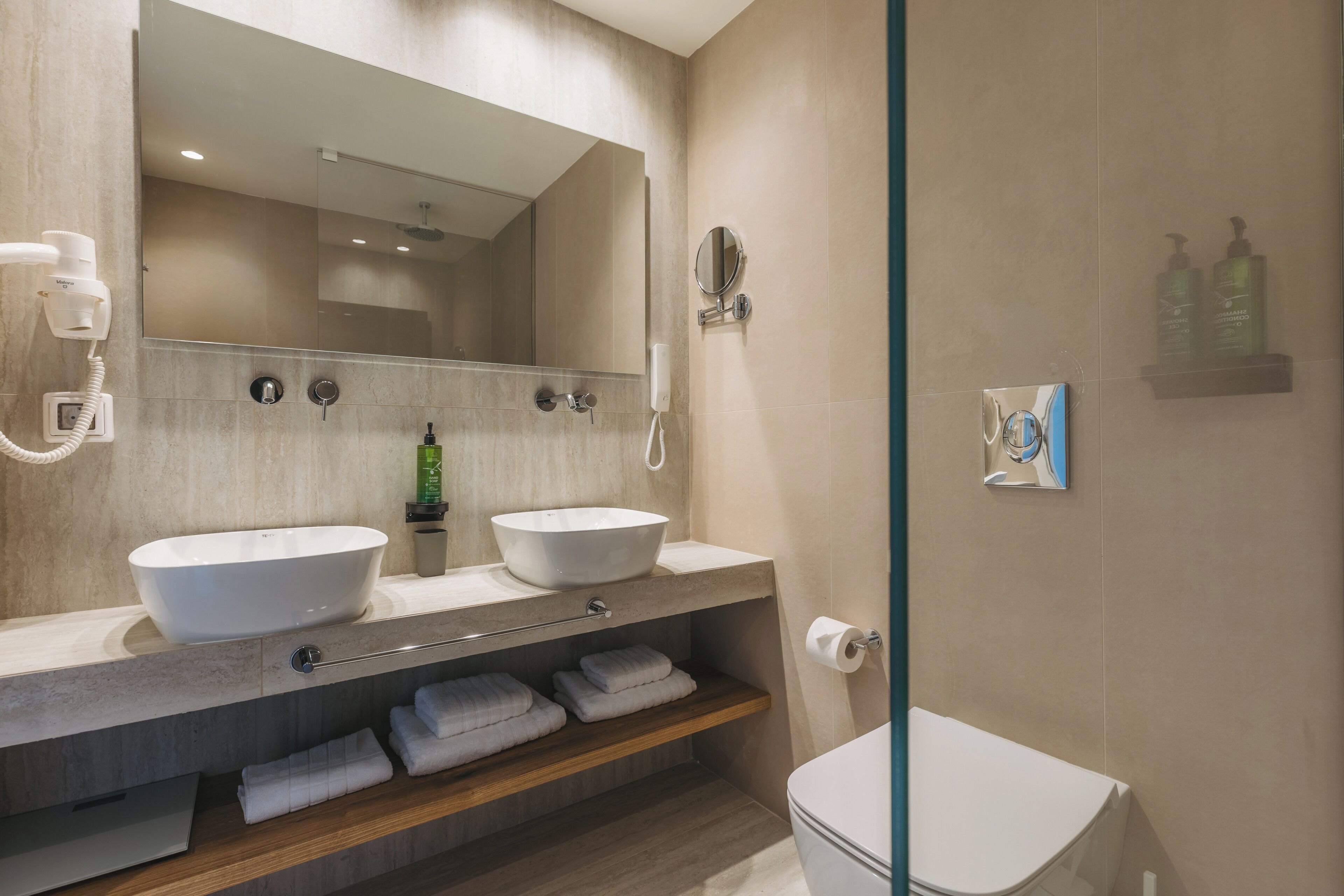 A modern bathroom with two sinks, a mirror, a toilet, and a shower area.