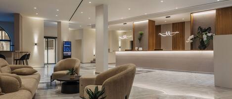 A modern hotel lobby with a reception desk, seating area, and a large mirror.