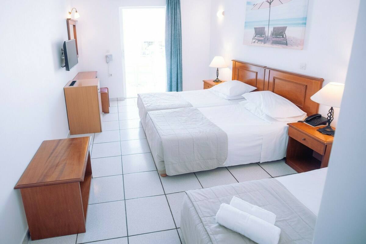 Une chambre d’hôtel avec deux lits, un bureau, une télévision, un téléphone et un tableau représentant une scène de plage.