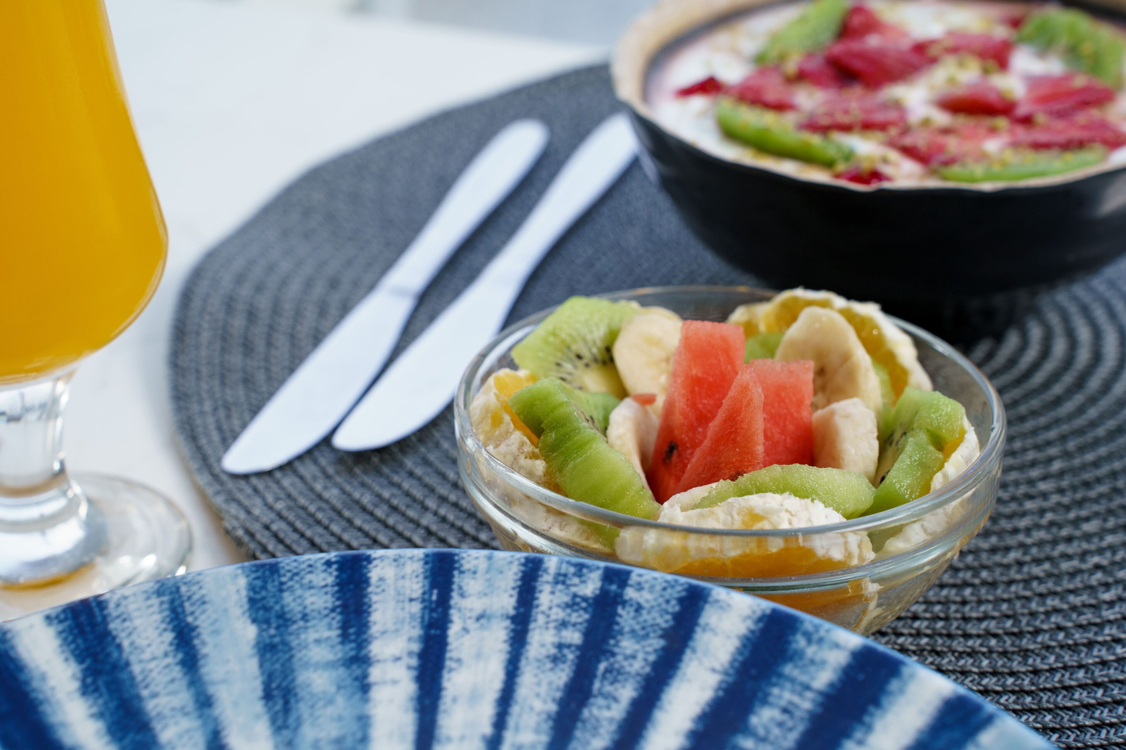 Un desayuno con un frutero, un vaso de zumo de naranja y un tazón de cereales.
