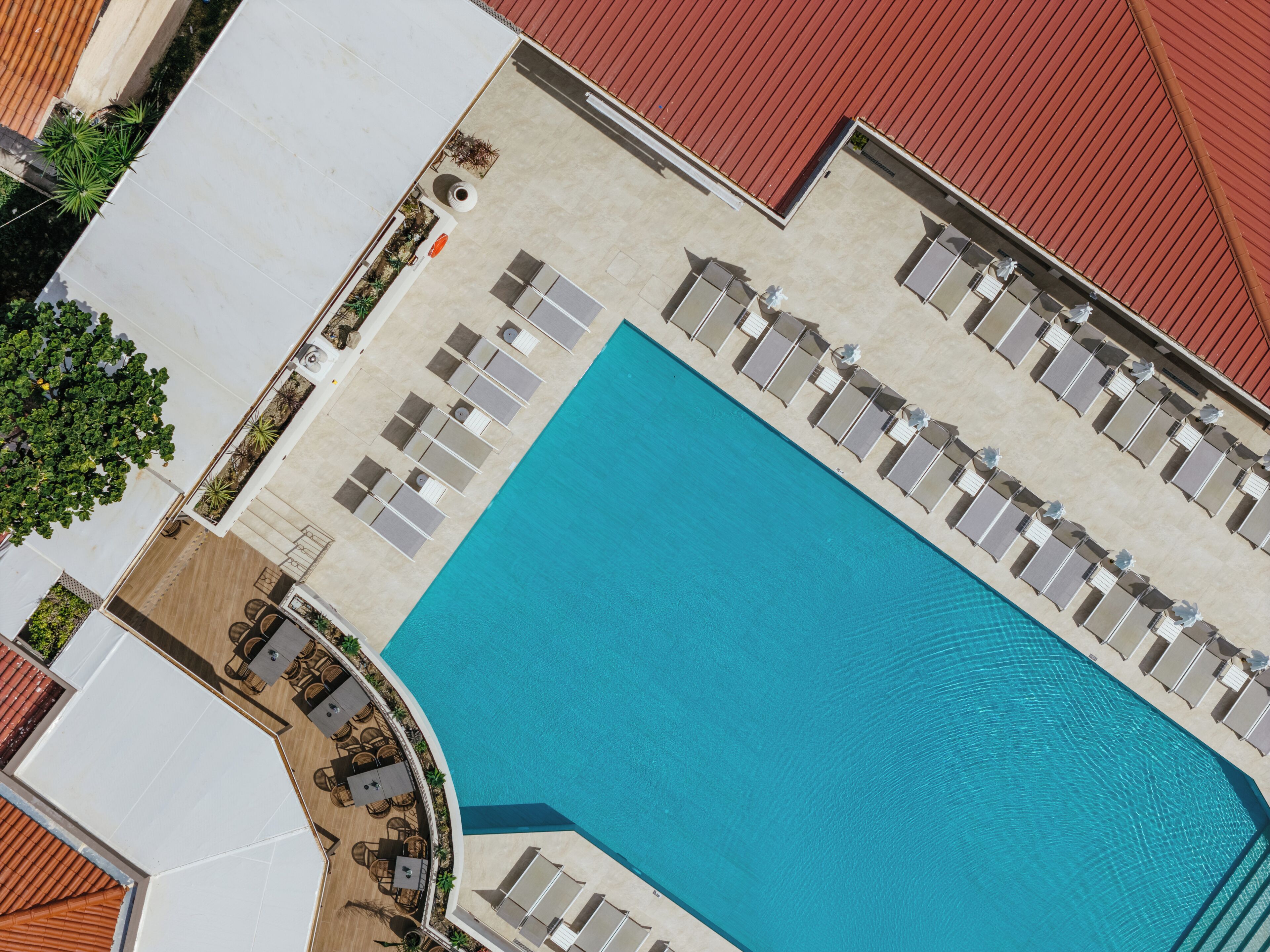Vista aérea de un hotel con una piscina rectangular grande rodeada de tumbonas y una zona de estar cubierta.