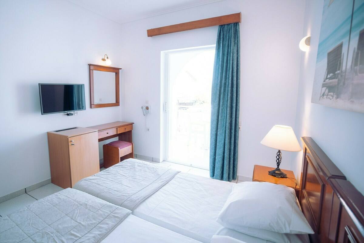 Une chambre d’hôtel équipée d’un lit, d’un bureau, d’une chaise, d’une télévision, d’une lampe et d’une fenêtre avec des rideaux.