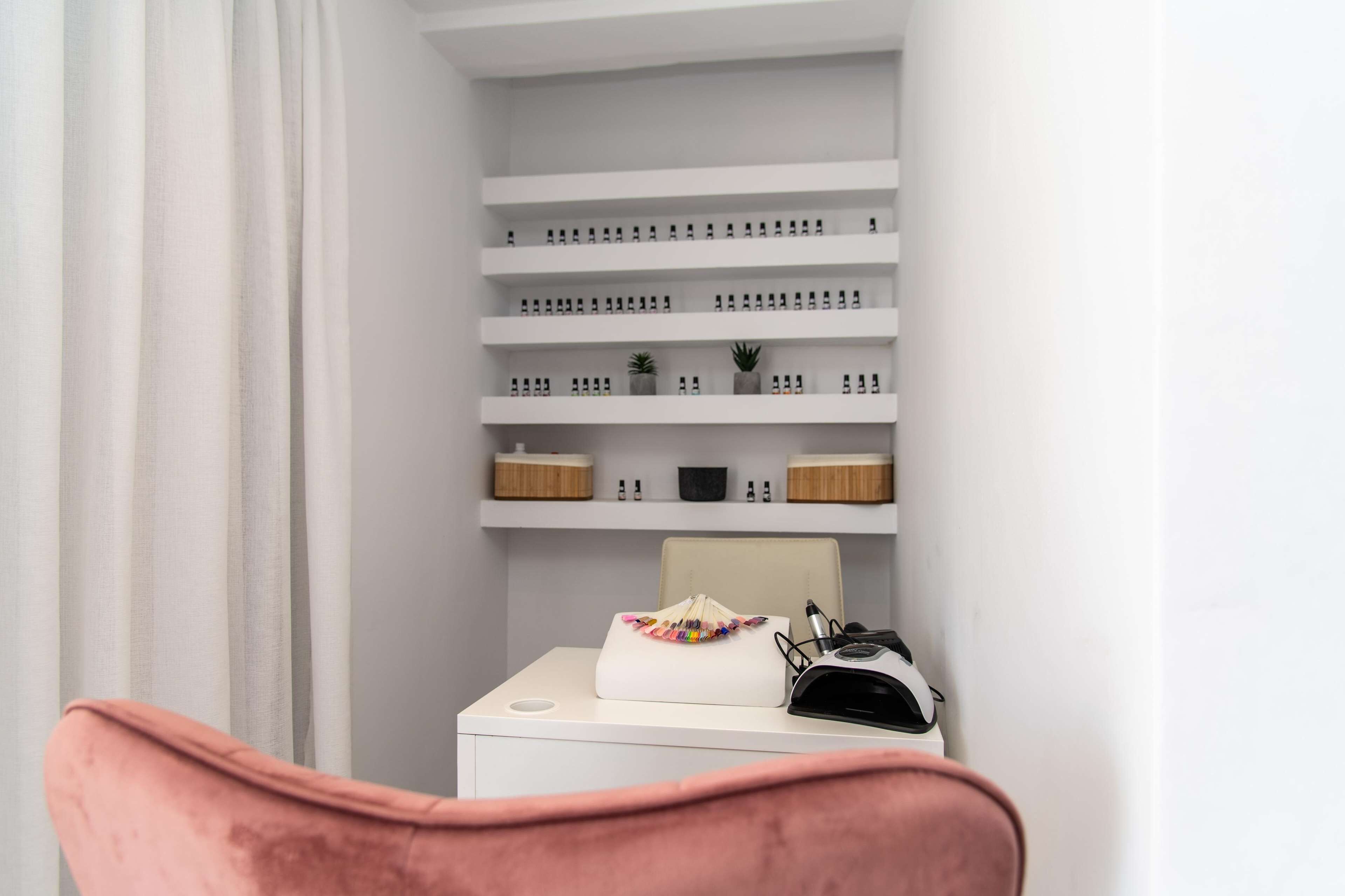 A neatly organized room with white shelves containing various items, a small table with a white bag and a black object, and a pink chair.