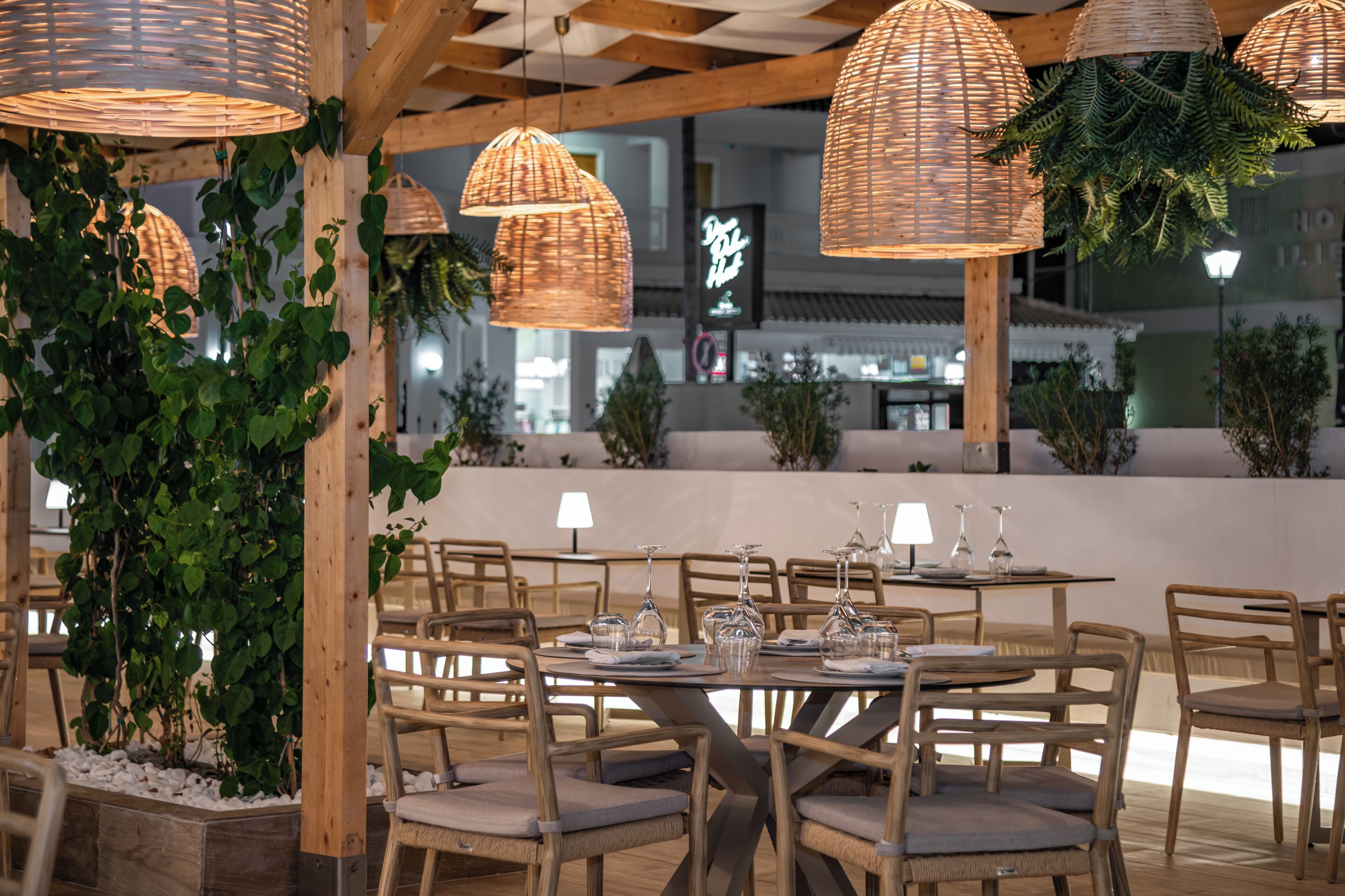 An outdoor dining area with wicker pendant lights, wooden chairs, and tables set for dining.