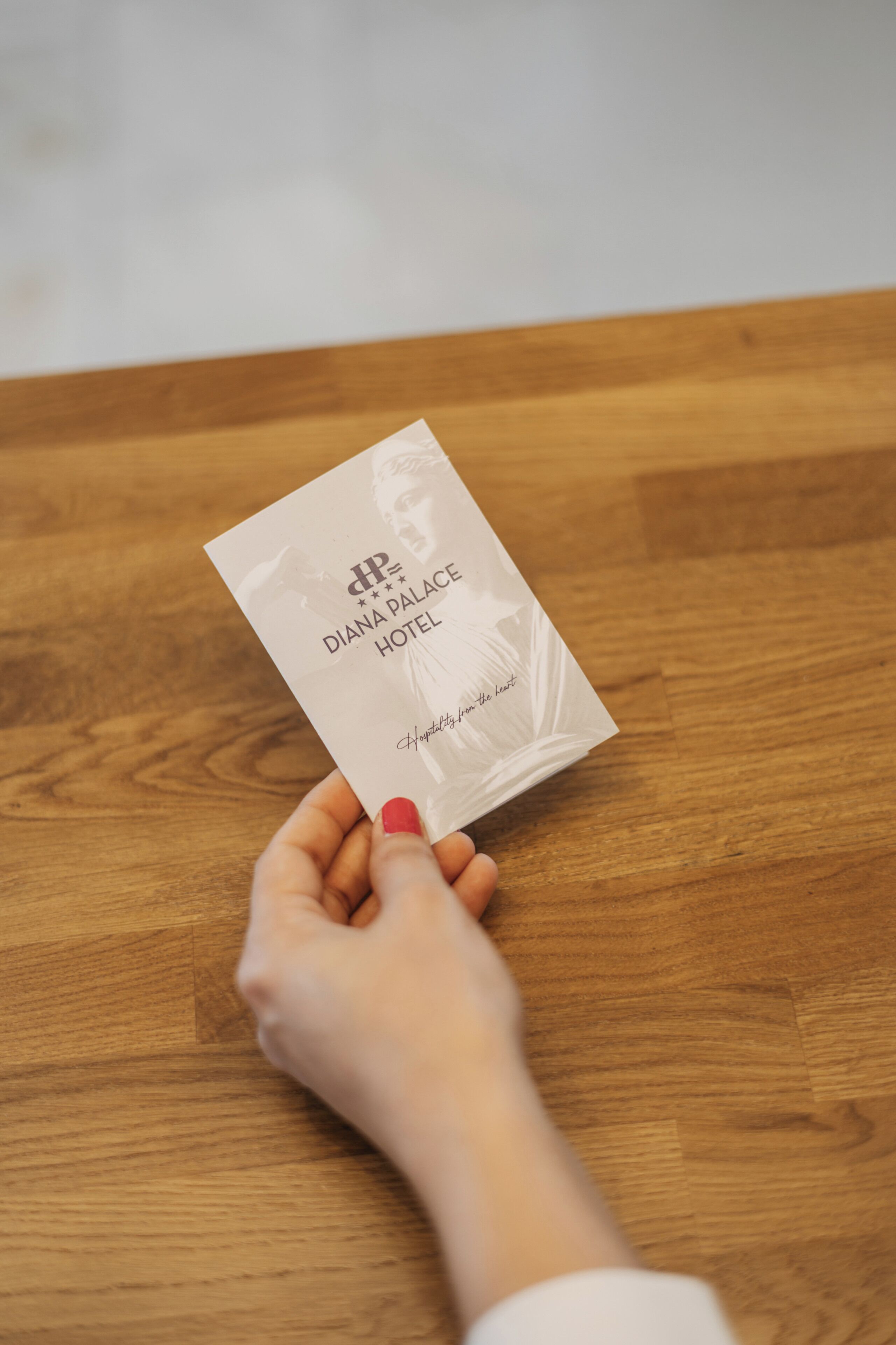 A hand holding a business card for the Diana Palace Hotel.