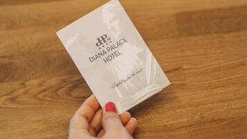 A hand holding a business card for the Diana Palace Hotel.