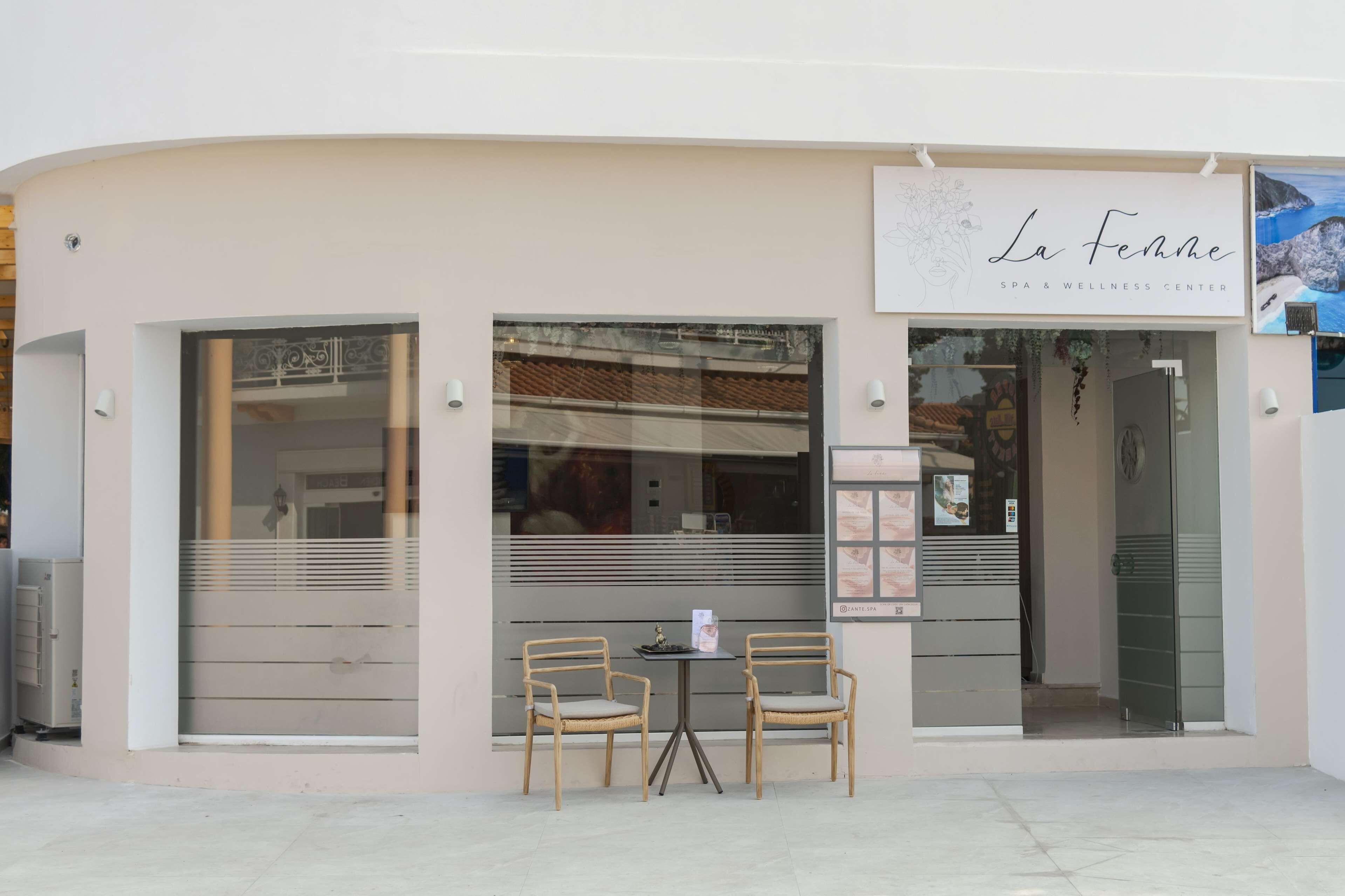 Un centro de spa y bienestar llamado "La Femme", con fachada moderna, amplias ventanas y una pequeña zona de estar al aire libre con dos sillas.