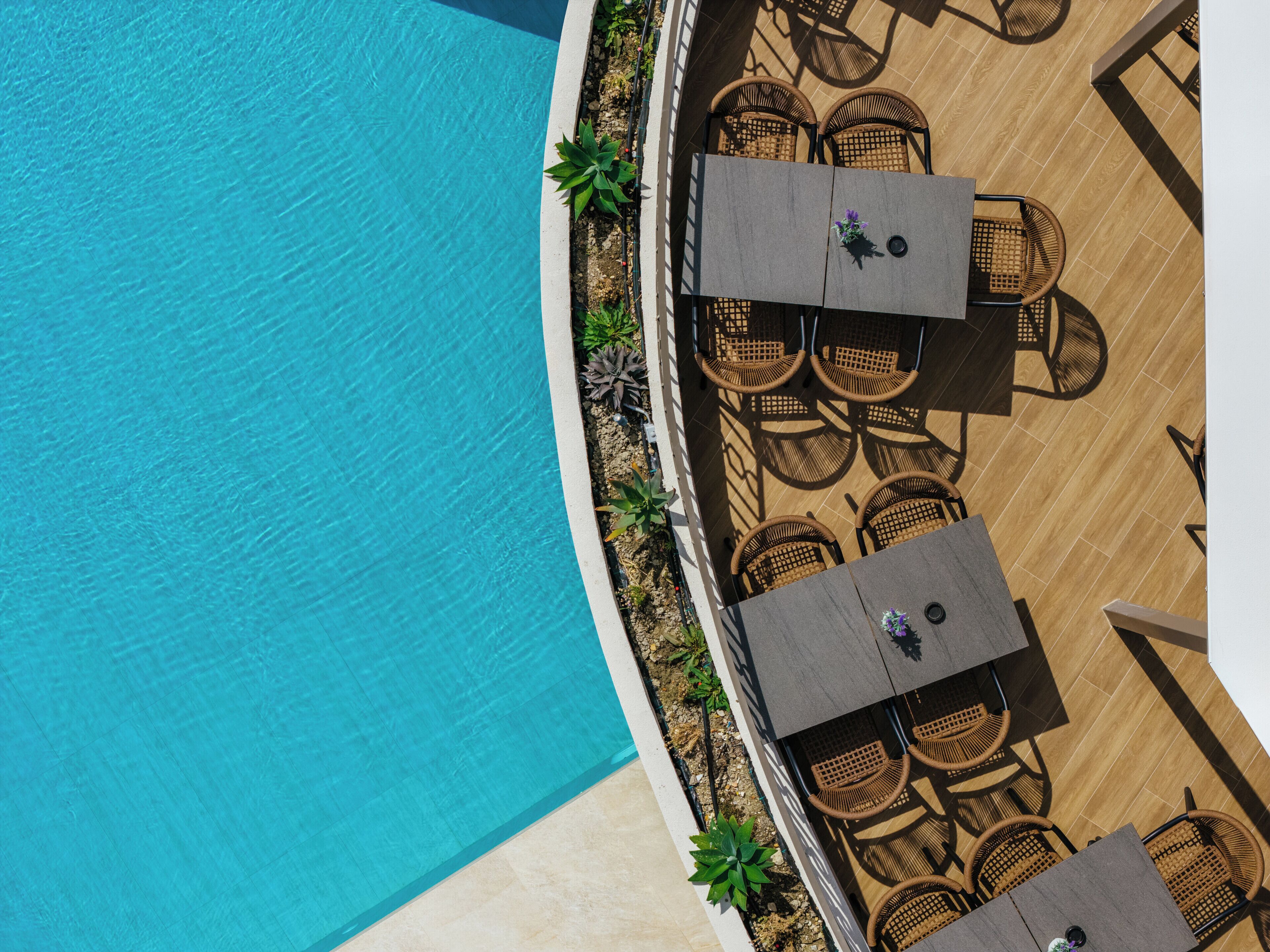 Vista aerea di una zona piscina con un solarium in legno, sedie e tavoli in vimini.