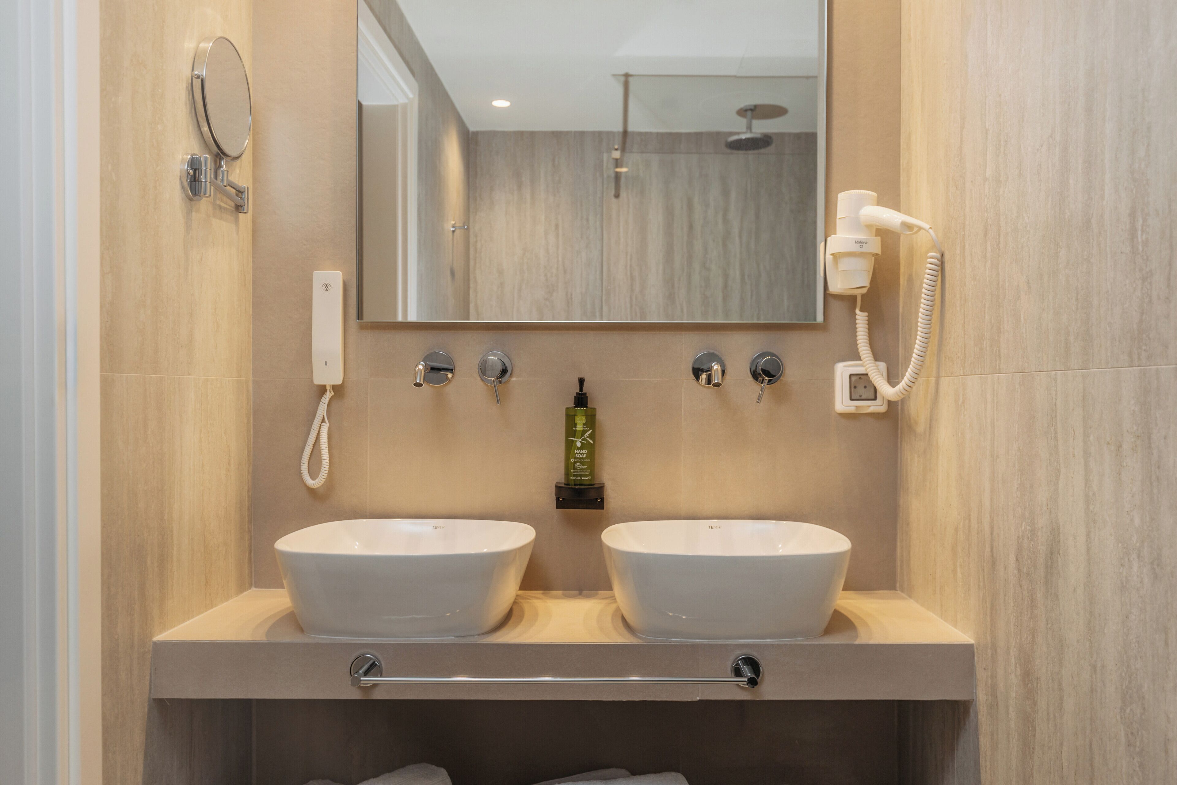 A bathroom with two sinks, a mirror, a hairdryer, and a shower.