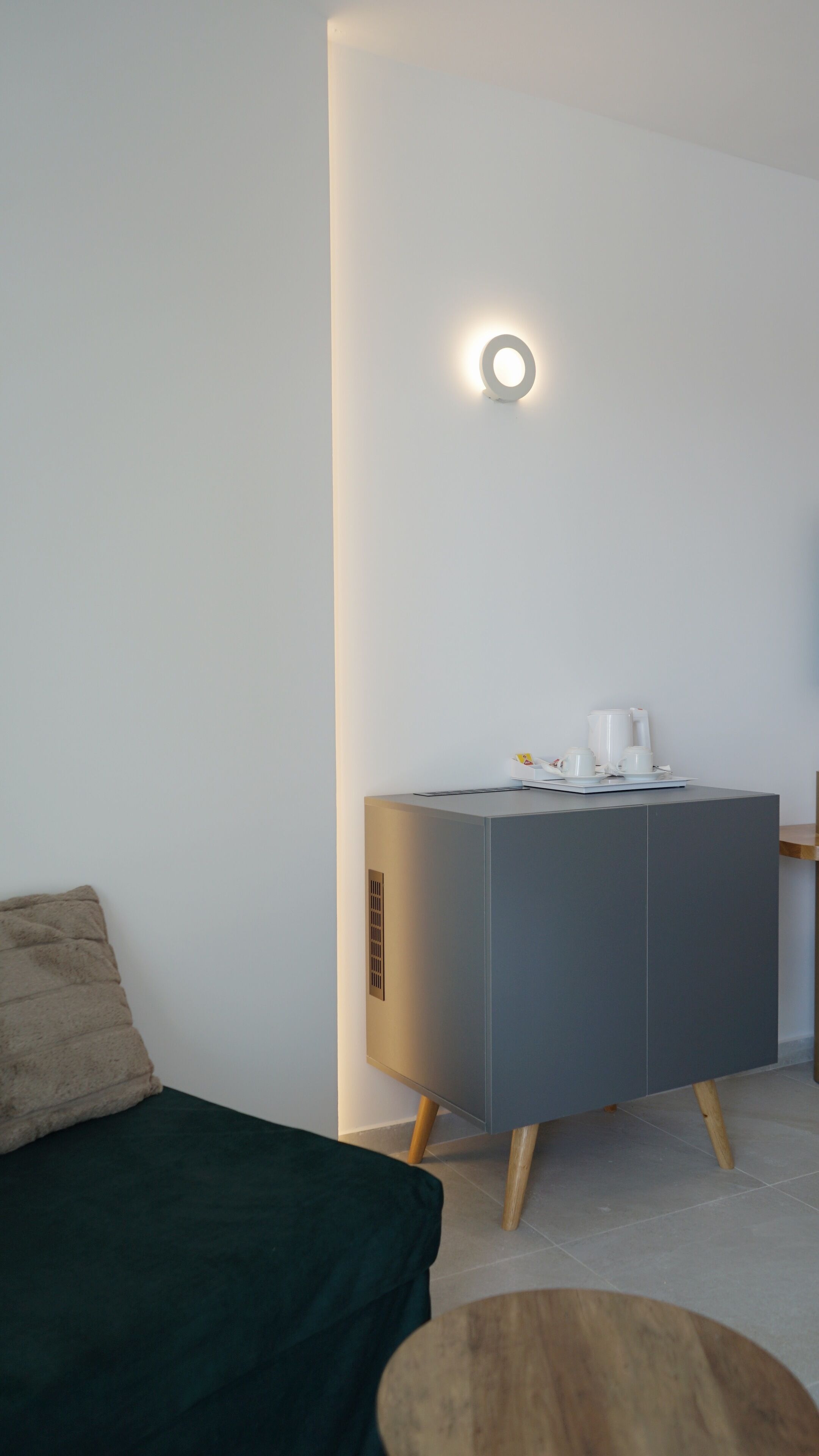 Una habitación moderna y minimalista con una consola gris, un sofá verde y una mesa redonda de madera.