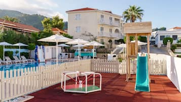 A pool area with a slide, a swing set, and umbrellas.