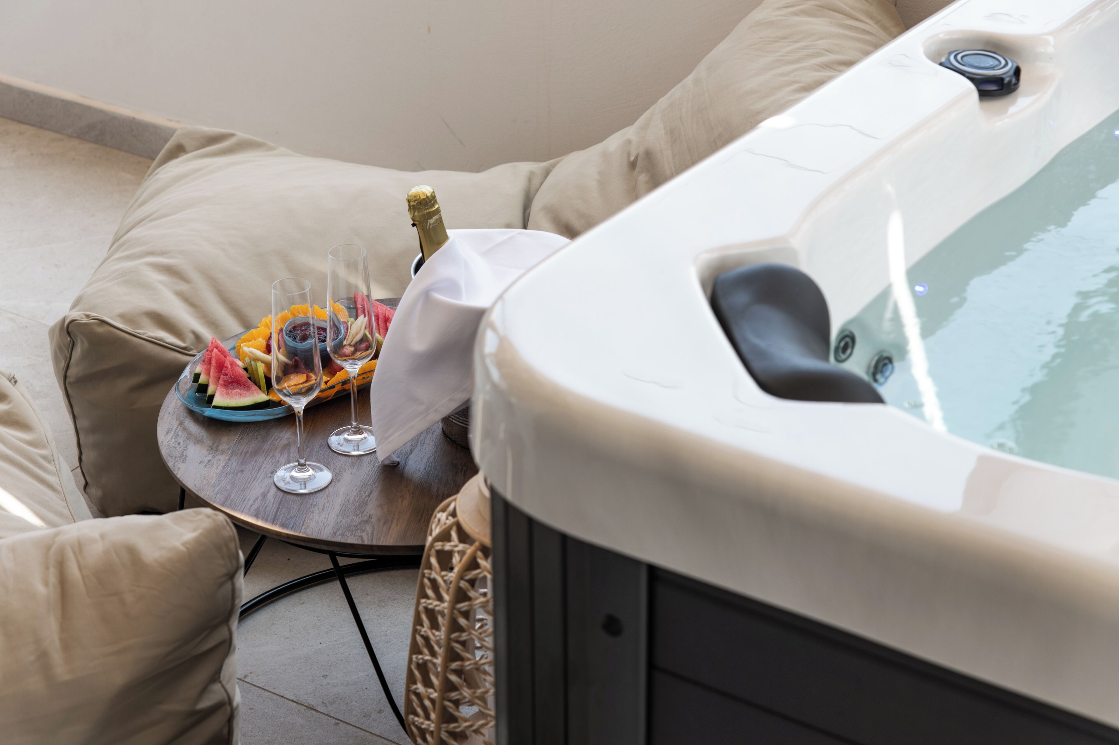 A hot tub, a glass of wine, and a fruit platter on a small table.