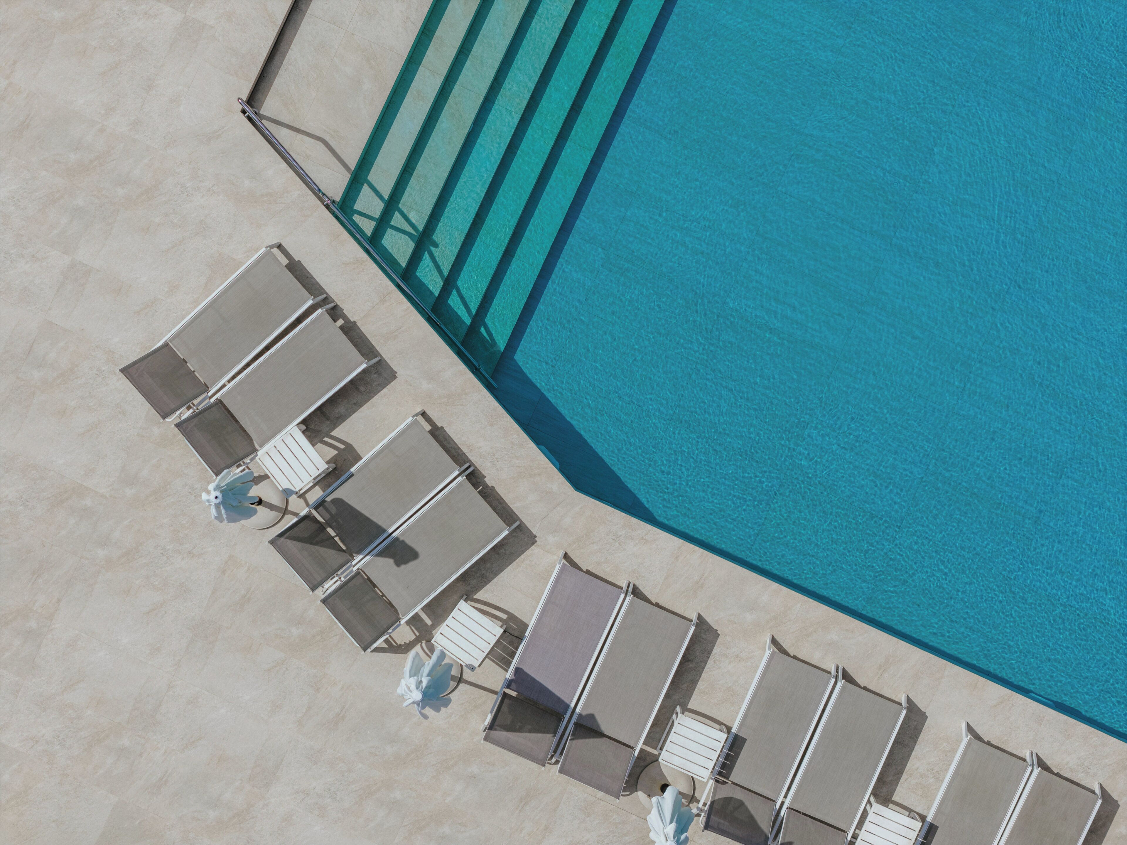 An aerial view of a pool area with multiple sun loungers and a clear blue pool.