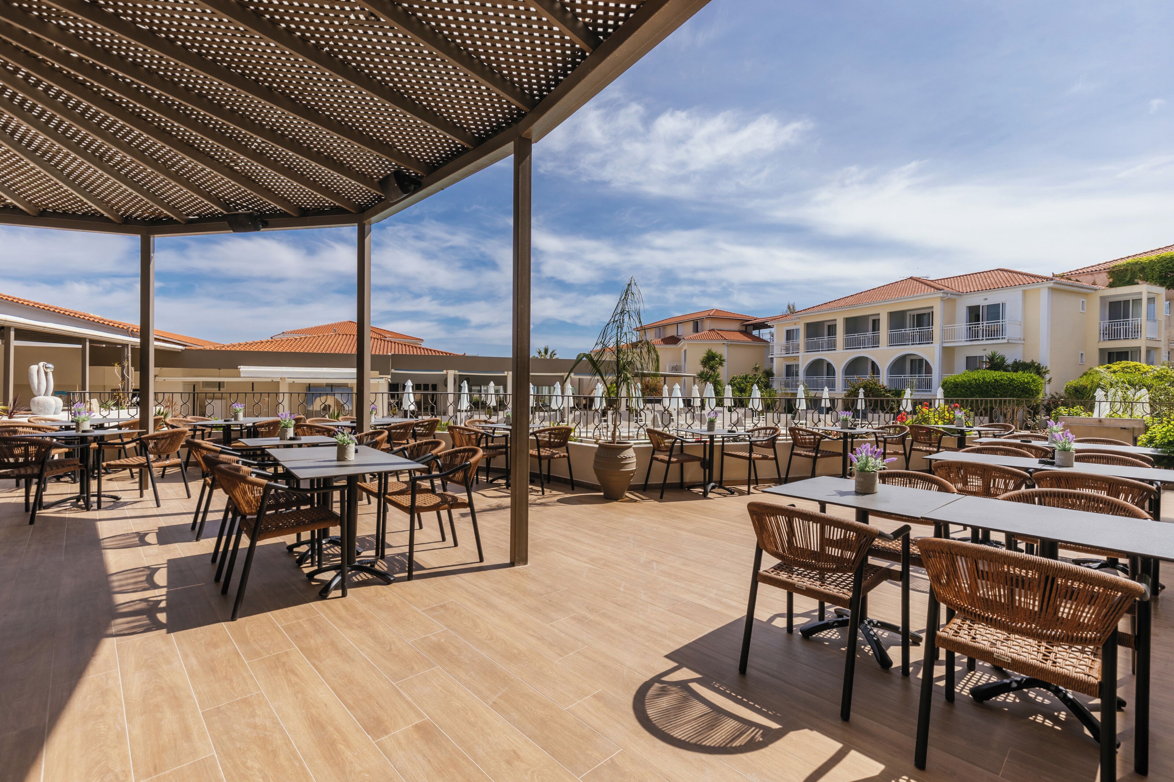 An outdoor patio area with tables and chairs, a pergola, and a view of buildings in the background.