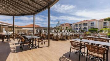 An outdoor patio area with tables and chairs, a pergola, and a view of buildings in the background.