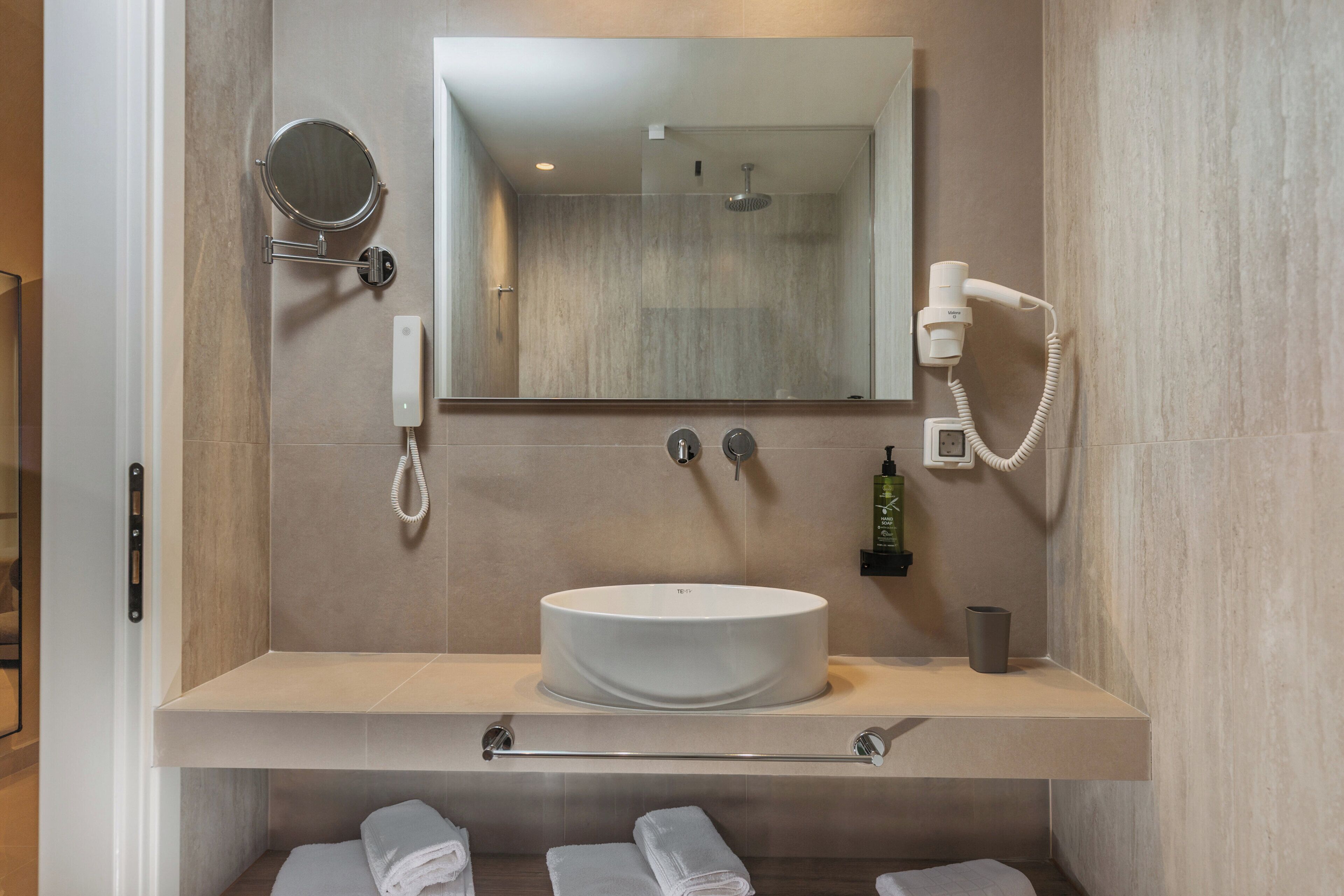Une salle de bain moderne avec un grand miroir rond, un lavabo encastré, une douchette à main et un sèche-cheveux.