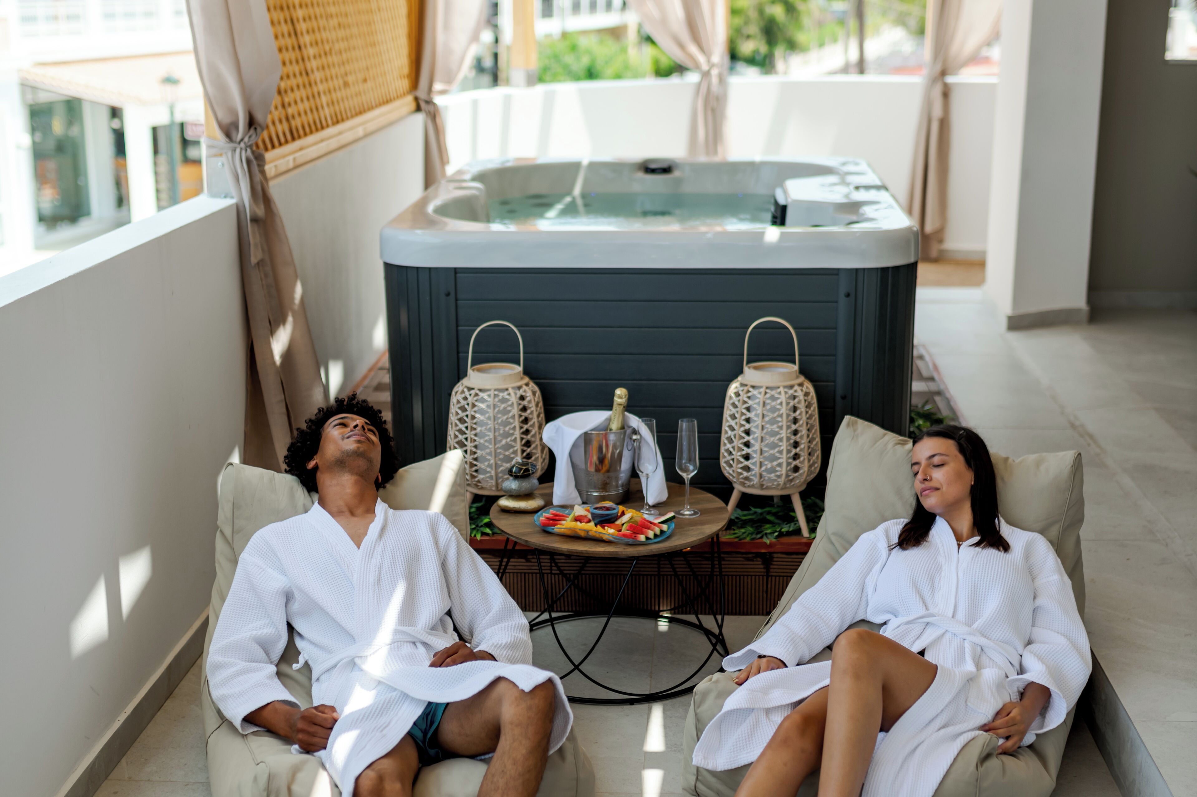 Dos personas relajándose en un ambiente de spa con un jacuzzi y dos faroles decorativos.