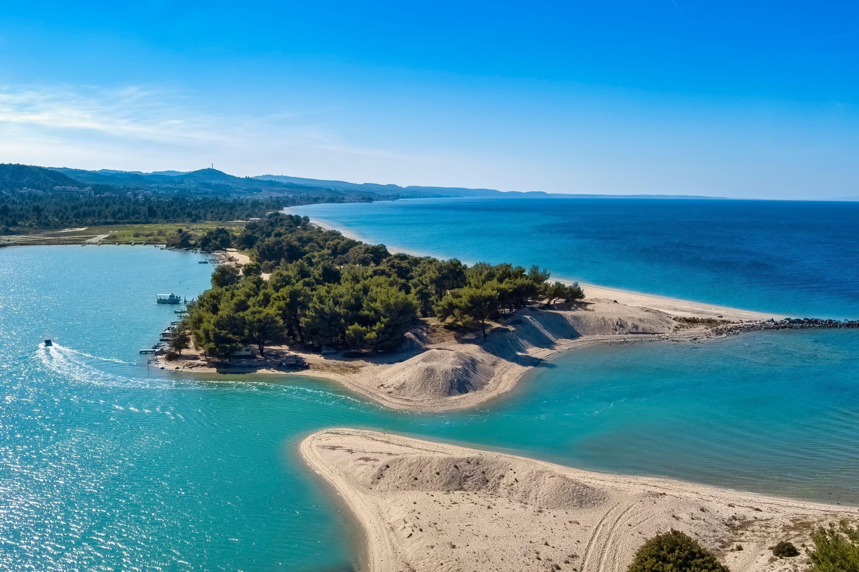 An aerial view of a coastal area with a sandy beach, clear turquoise waters, and a small island with dense greenery.