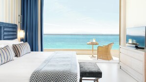A hotel room with a large bed, a television, a small table with a candle, and a view of the ocean. - Ikos Oceania - All Inclusive (Nea Propontida)