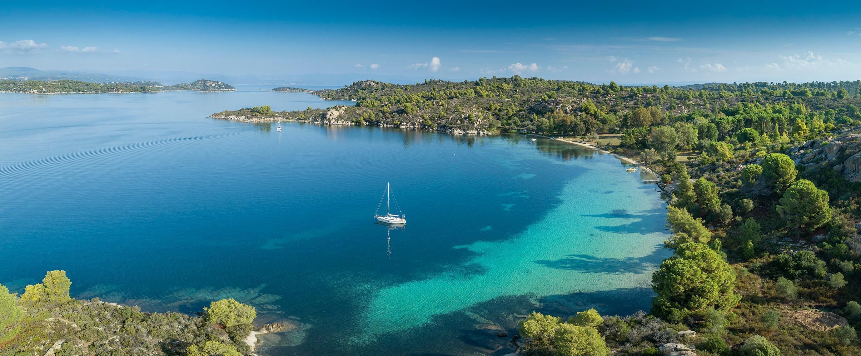 Una zona costera con mar azul turquesa, un pequeño barco anclado cerca de la orilla y un paisaje boscoso.