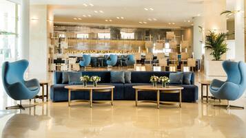 A modern lobby with a blue sofa, two round tables with vases, and a bar area in the background.